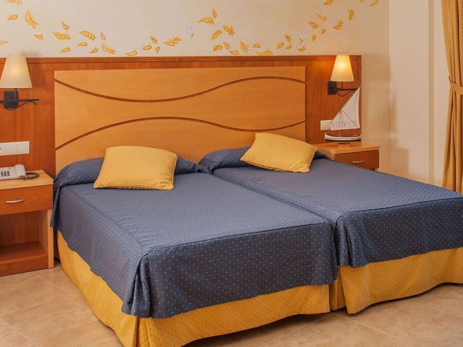 A double bed with two pillows, a wooden headboard, bedside lamps, a nightstand, and a wall with leaf decals.