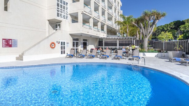 A swimming pool with lounge chairs and a building with balconies. - Golden Acqua Salou (Salou)