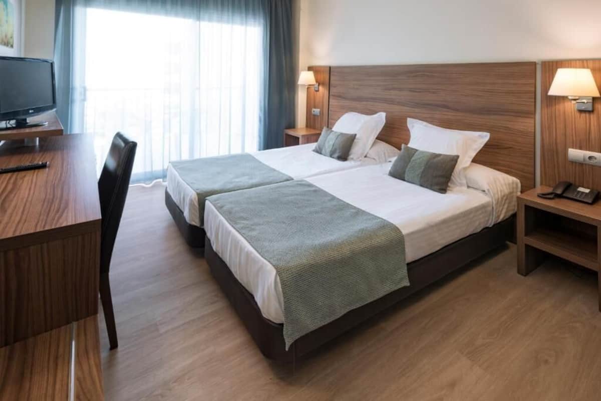 Habitación de hotel con dos camas, un escritorio, un televisor y una ventana con cortinas.