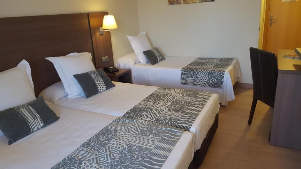 Habitación de hotel con dos camas, un escritorio, una silla y una mesita de noche con lámpara.