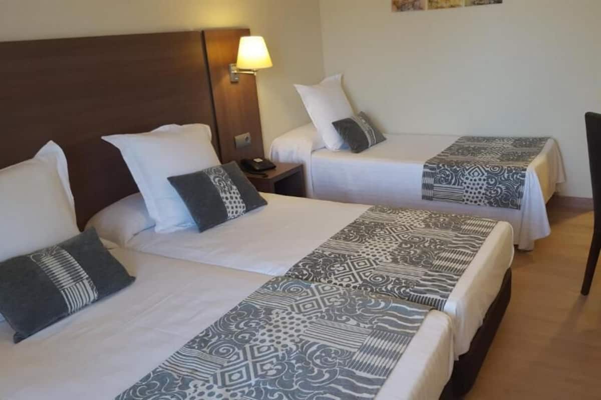Habitación de hotel con dos camas, un escritorio, una silla y una mesita de noche con lámpara.