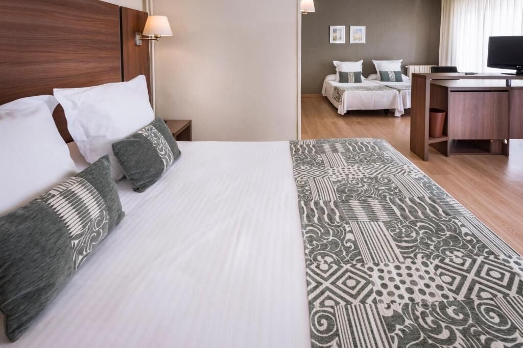 Habitación de hotel con una cama, dos mesitas de noche, un escritorio, una silla y un televisor.
