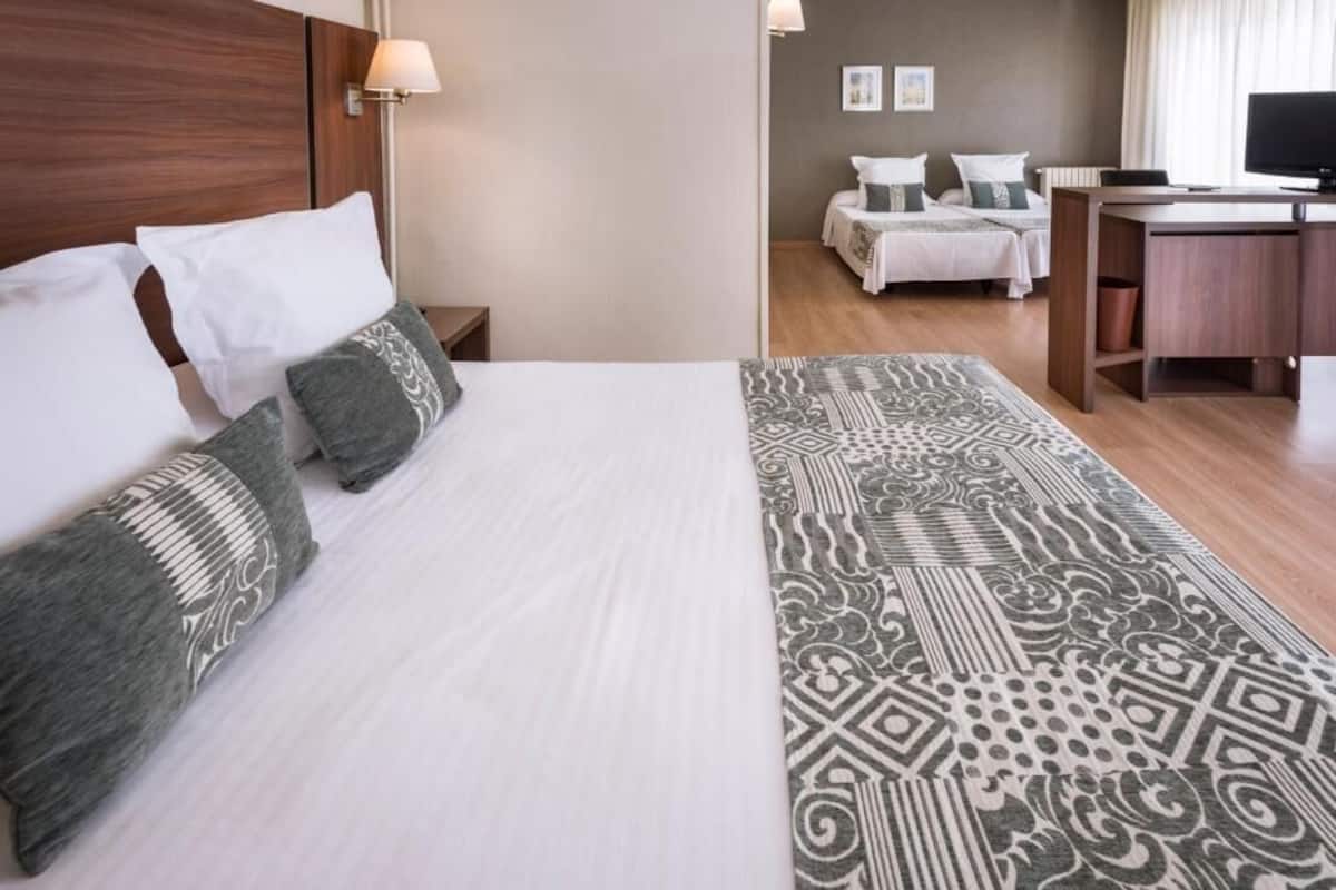 Habitación de hotel con una cama, dos mesitas de noche, un escritorio, una silla y un televisor.