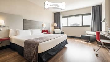 Ett modernt hotellrum med en stor säng, ett skrivbord med en stol, en skrivbordslampa och utsikt över staden genom fönstret.