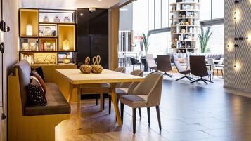 A modern interior with a wooden dining table, cushioned seating, and a bookshelf filled with decorative items.