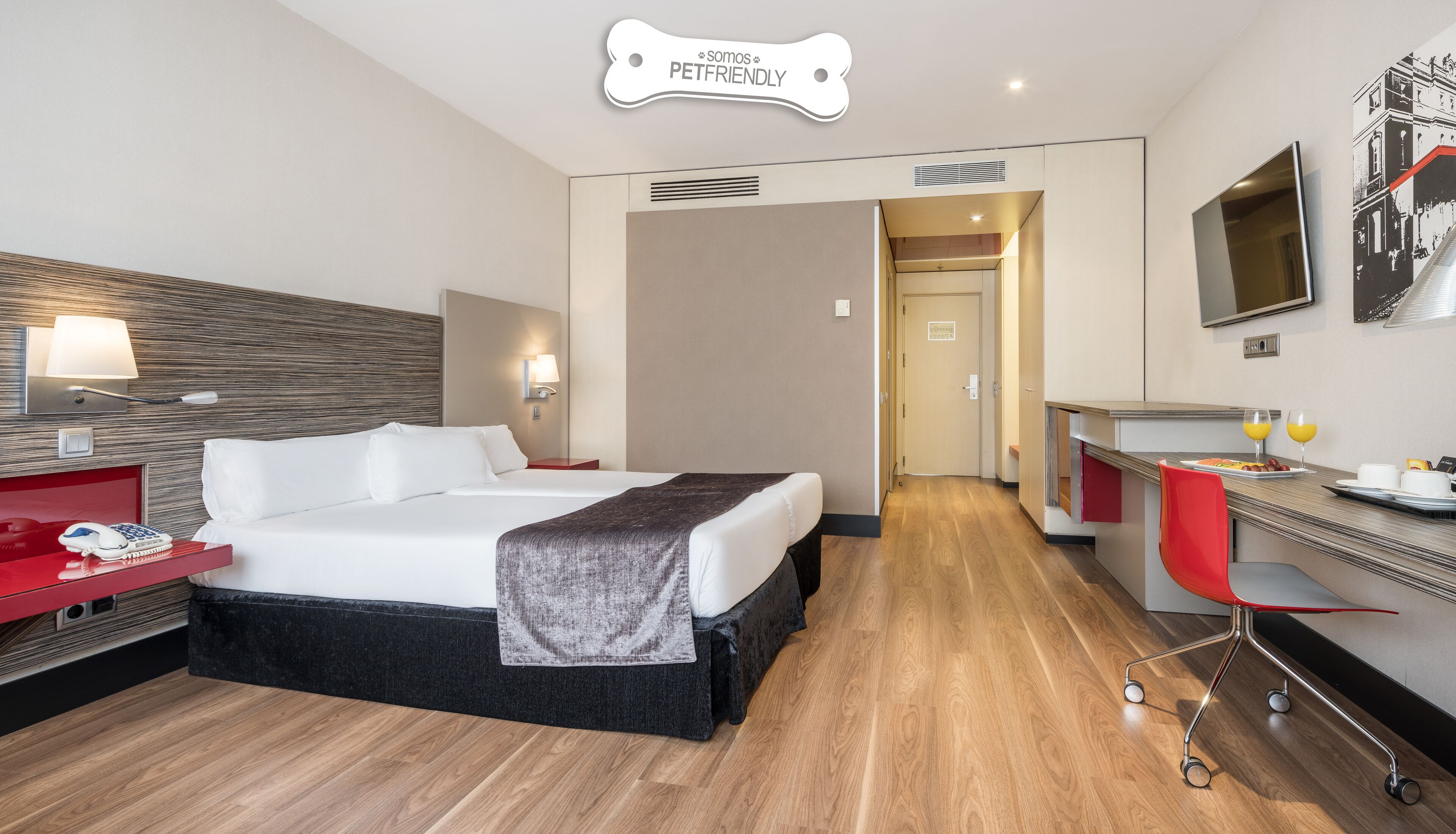 A hotel room with a bed, bedside table, lamp, and a desk with a chair.