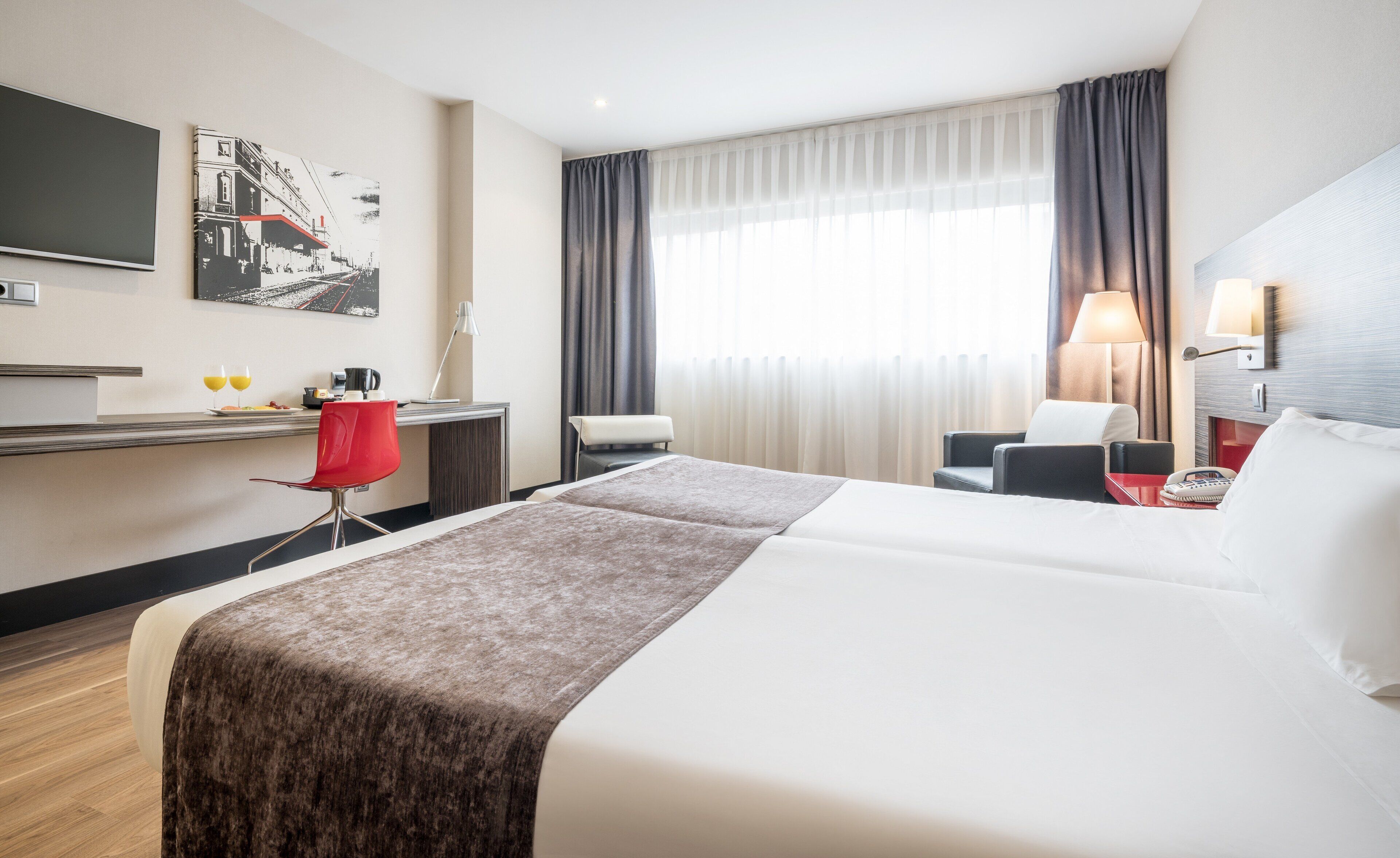 Een hotelkamer met een bed, een bureau, een stoel, een televisie en een raam met gordijnen.
