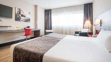 Een hotelkamer met een bed, een bureau, een stoel, een televisie en een raam met gordijnen.