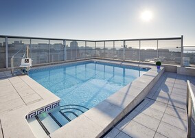 Una piscina en la azotea con agua cristalina, una silla accesible para sillas de ruedas y vistas a la ciudad.