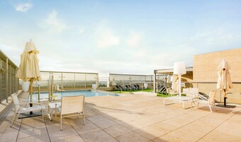 Un área de piscina en la azotea con sillones, sombrillas y una alberca.