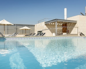 A swimming pool with lounge chairs and umbrellas, a covered seating area, and a tall chimney.