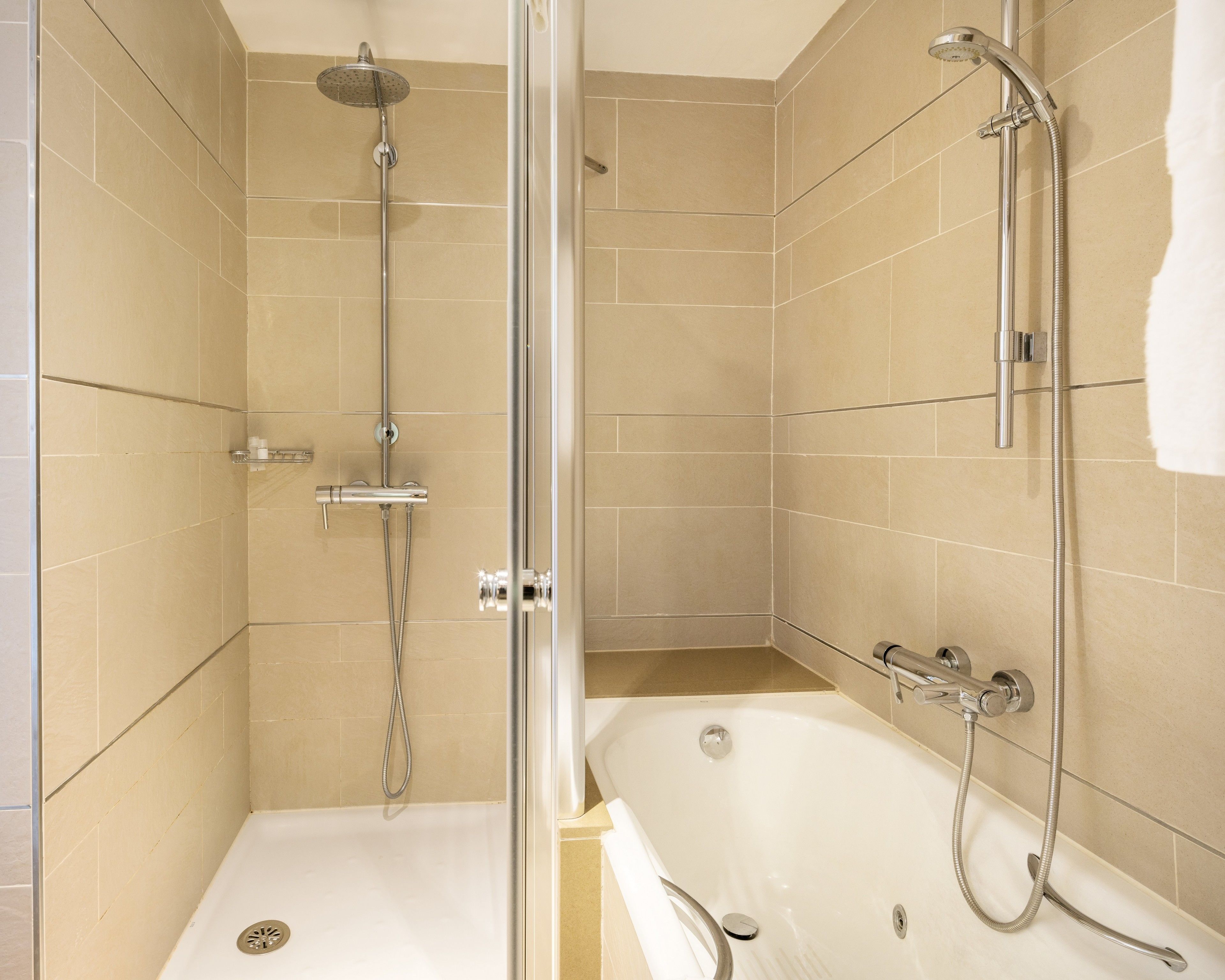 Un baño moderno con ducha acristalada, bañera y paredes con azulejos color beige.