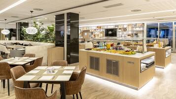 Restaurante moderno com área de buffet central, mesas e cadeiras para acomodação, e um arranjo decorativo de plantas.