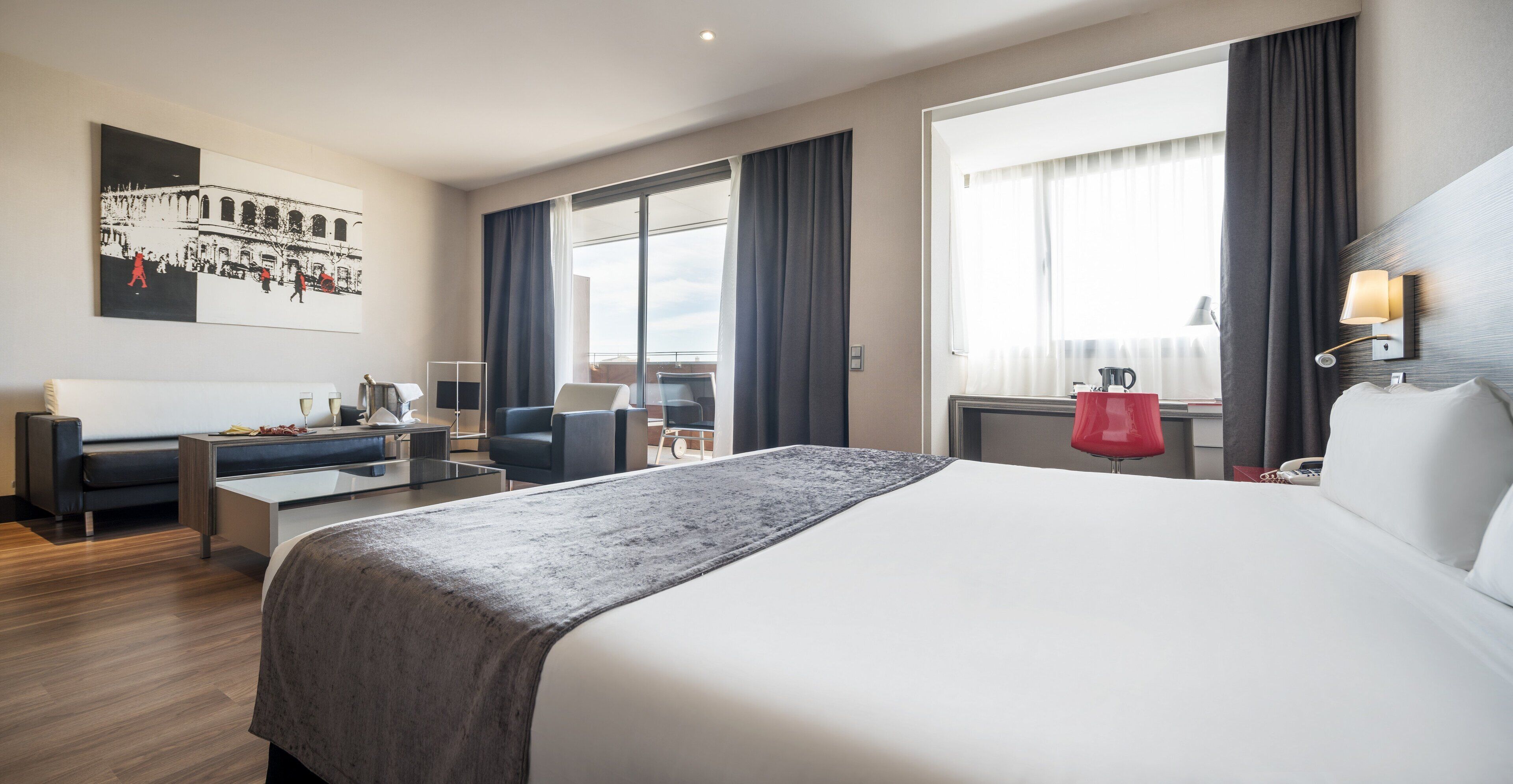 Una habitación de hotel moderna con una cama grande, un escritorio, un sofá y un balcón con cortinas.