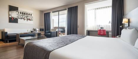 Una habitación de hotel moderna con una cama grande, un escritorio, un sofá y un balcón con cortinas.
