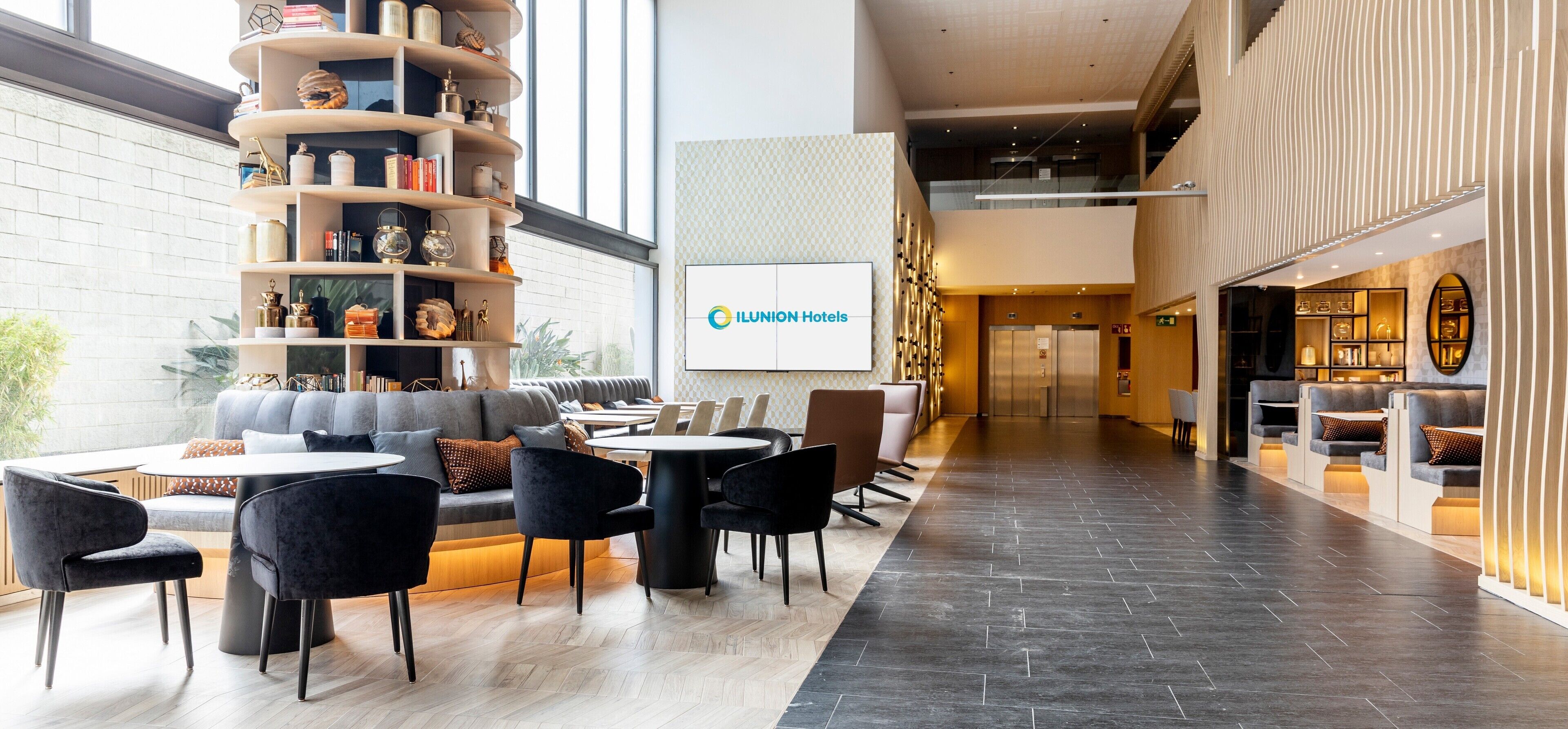 Un moderno vestíbulo de hotel con una zona de estar, un mostrador de recepción y un gran cartel de ILUNION Hotels.