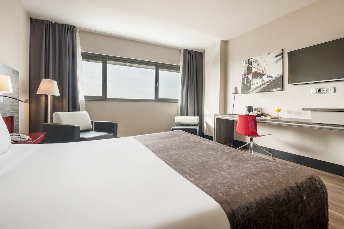 A hotel room with a large bed, a desk with a chair, a TV, and a window with curtains.