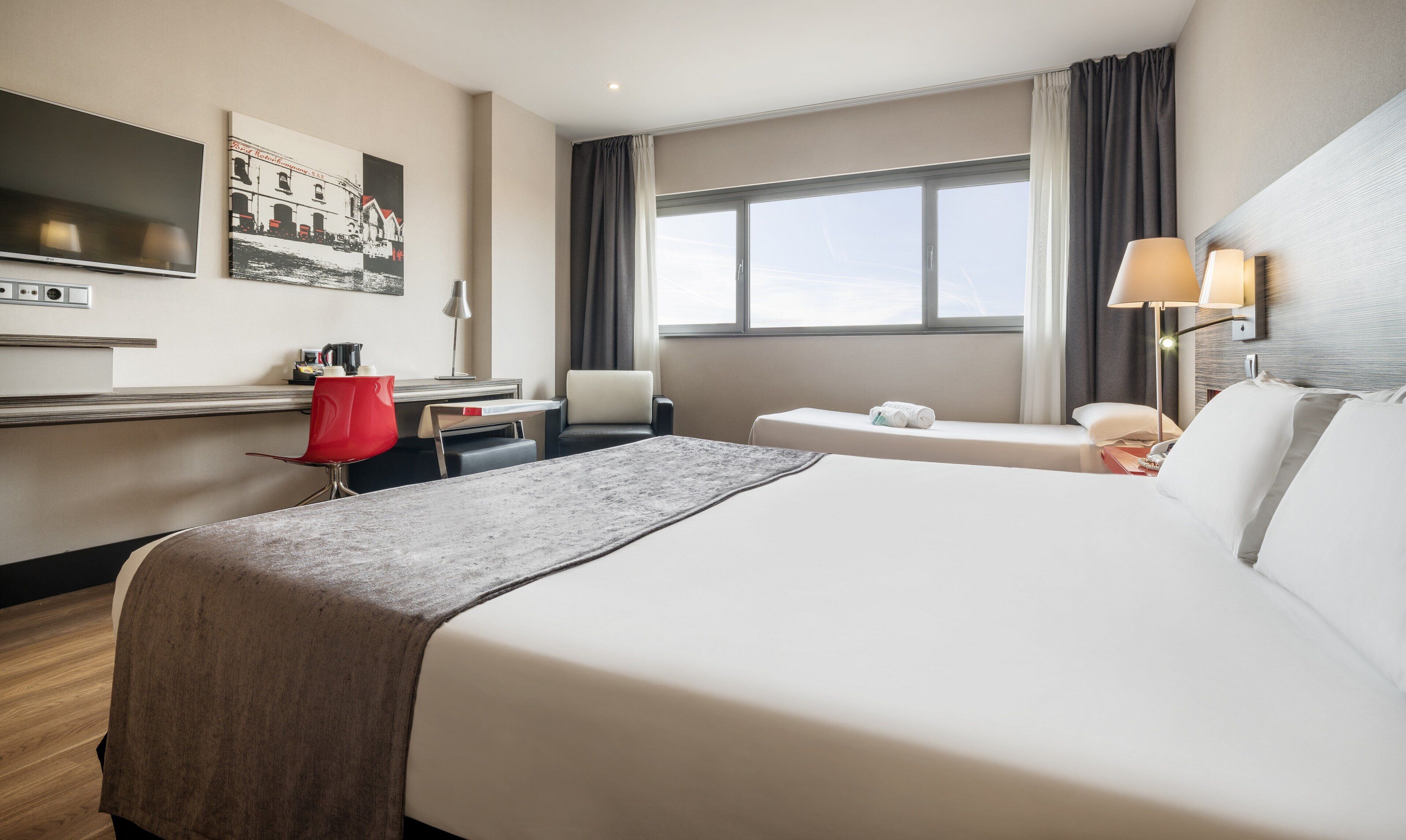 Une chambre d’hôtel avec un grand lit, un bureau avec une chaise, une télévision et une fenêtre avec des rideaux.