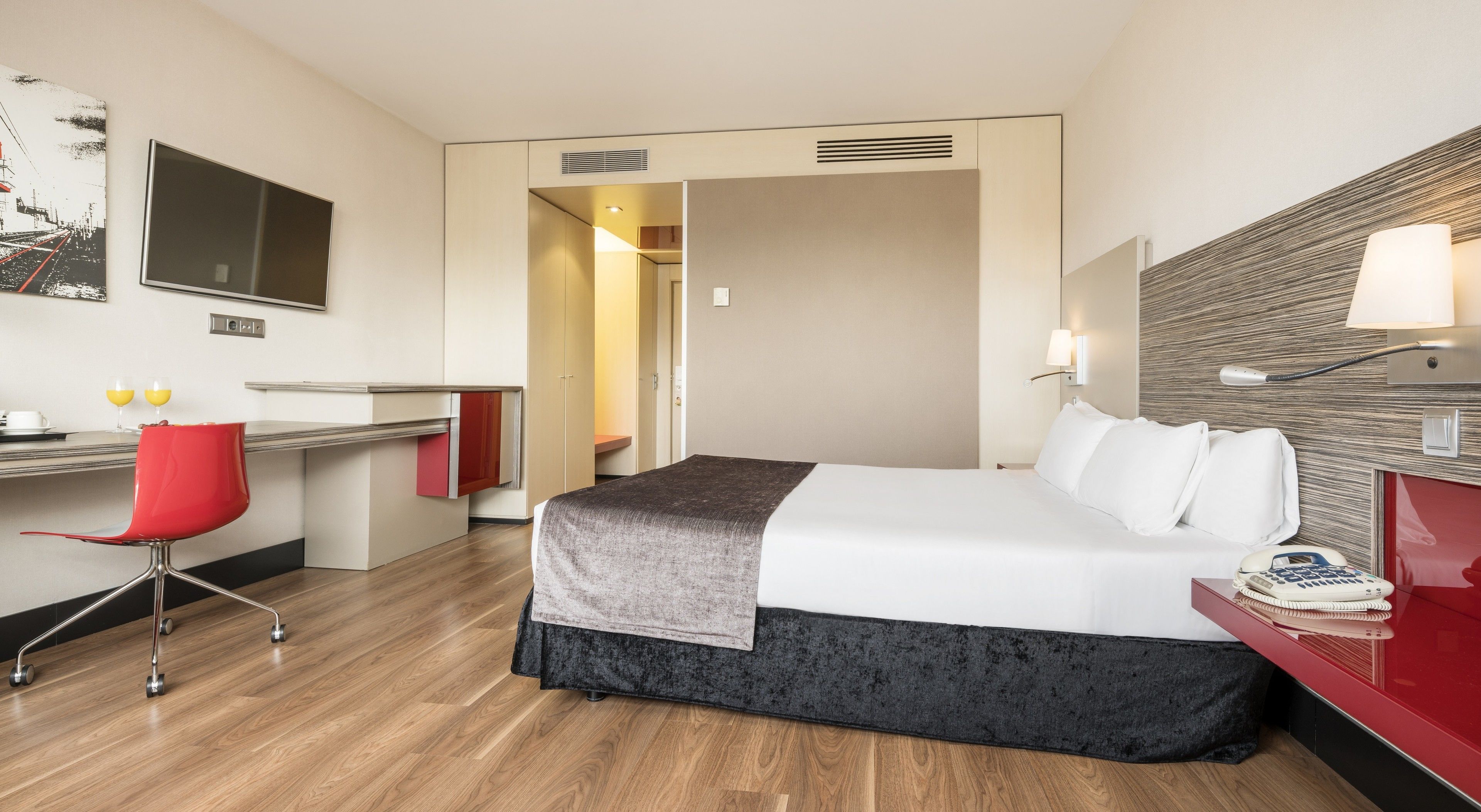 Quarto de hotel com cama, escrivaninha, cadeira e televisão.