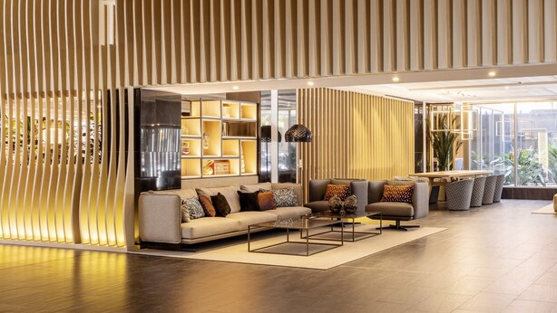 Un interior moderno con un sofá, sillones y una mesa de centro en una habitación luminosa, con una pared de acento de madera y un mensaje de bienvenida.