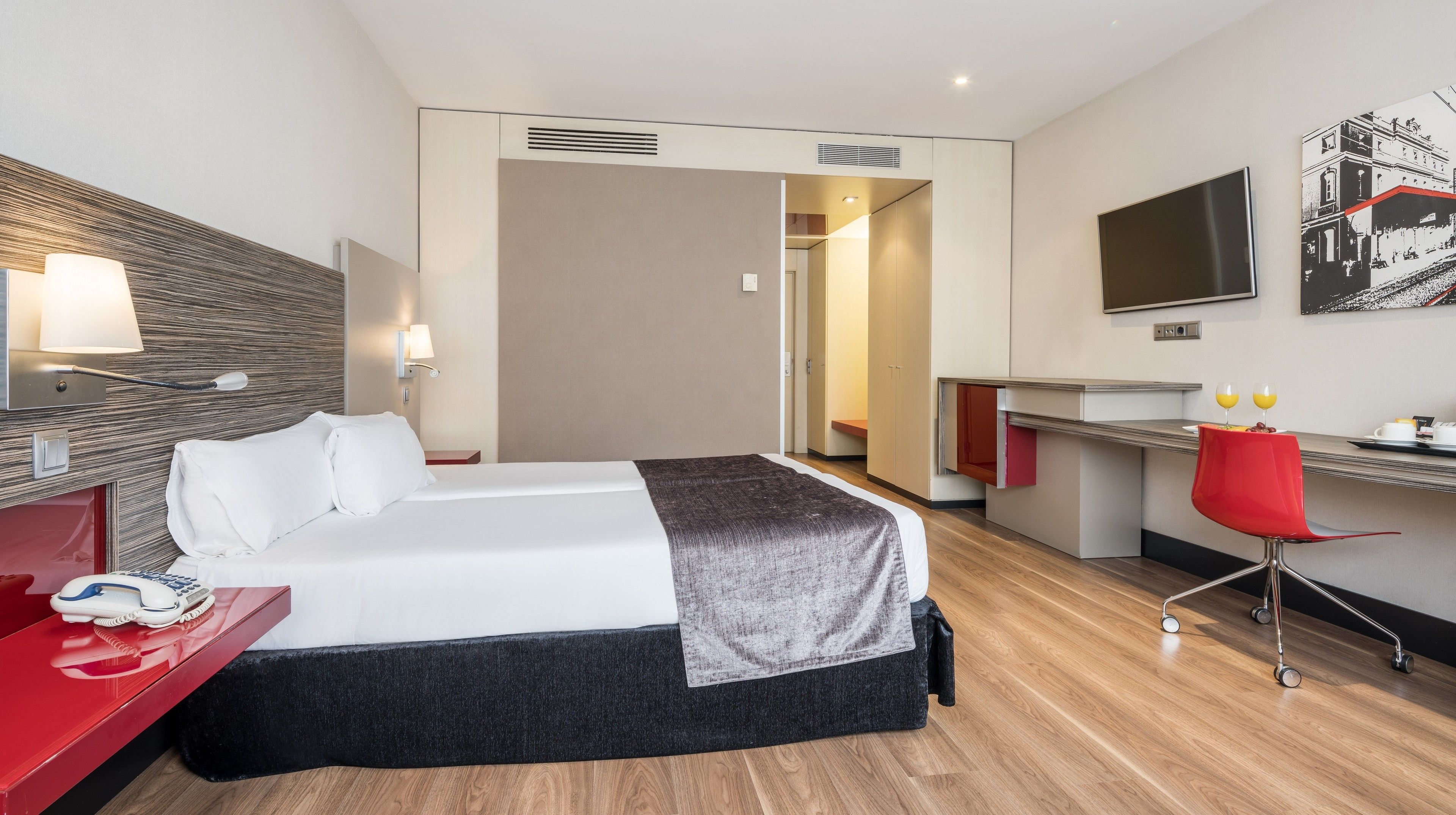 A hotel room with a bed, a desk, a chair, a TV, and a painting on the wall.
