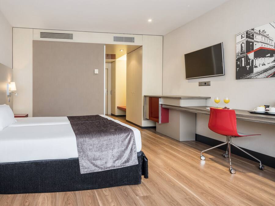 A hotel room with a bed, a desk, a chair, a TV, and a painting on the wall.