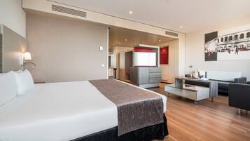 A modern hotel room with a large bed, a desk, a sofa, and a TV.