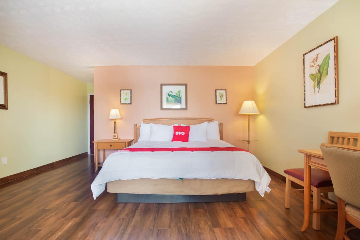 Habitación de hotel con cama, mesitas de noche, escritorio, silla y lámparas de pared.