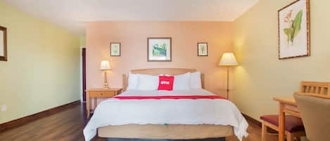 Habitació d'hotel amb llit, taules de nit, escriptori, cadira i làmpades penjades a la paret.