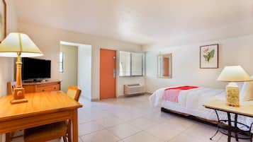 A hotel room with a bed, a desk, a chair, a television, and a window with blinds.