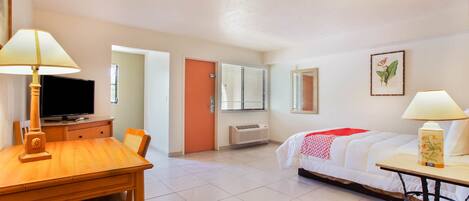 A hotel room with a bed, a desk, a chair, a television, and a window with blinds.