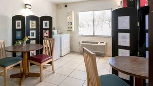 Una habitación pequeña y limpia con mesa, sillas, lavadora y ventana con persianas.