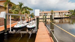 Un jet ski amarrado a un muelle de madera, con una masa de agua y un edificio al fondo.