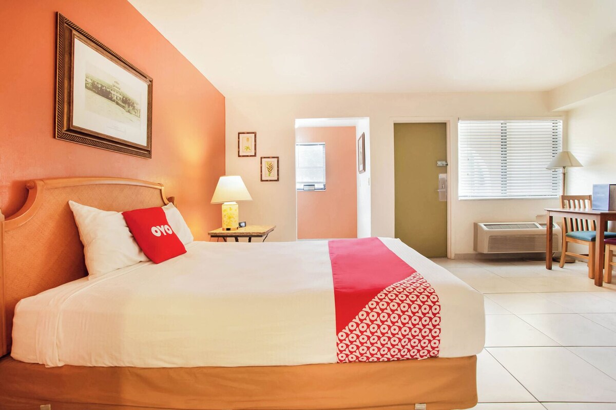 A hotel room with a bed, a desk, a chair, and a window with blinds.