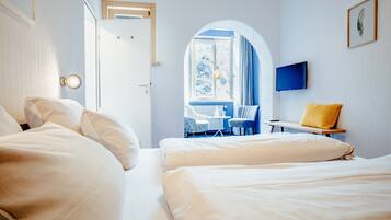 Habitación de hotel con dos camas, un televisor, una mesita y una ventana con vistas al exterior.