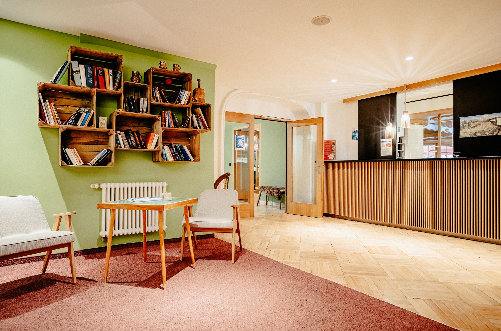 A modern room with a wooden floor, a white radiator, a wooden table with two chairs, and a bookshelf filled with books.
