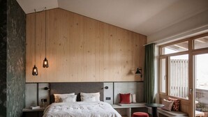 A modern bedroom with a wooden headboard, a bed with white bedding, a bench with cushions, and a small table.