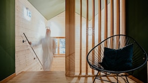 Een kamer met een houten vloer, een zwarte stoel met kussen en een houten scheidingswand met verticale latten.