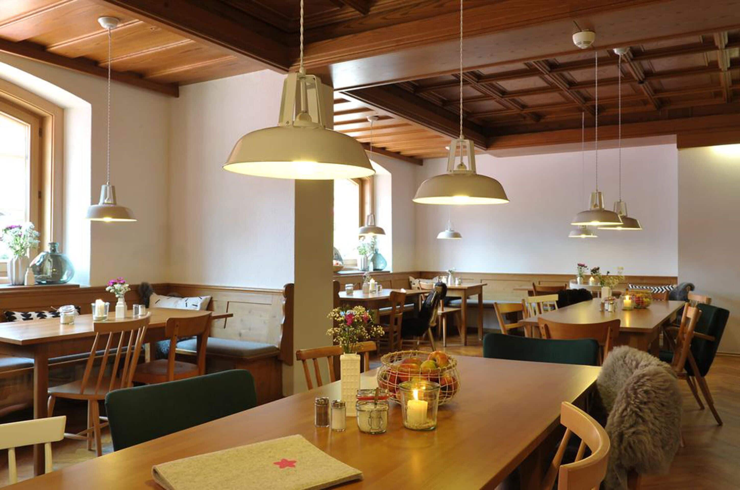 Un restaurante con mesas y sillas de madera, lámparas colgantes y un ambiente acogedor.