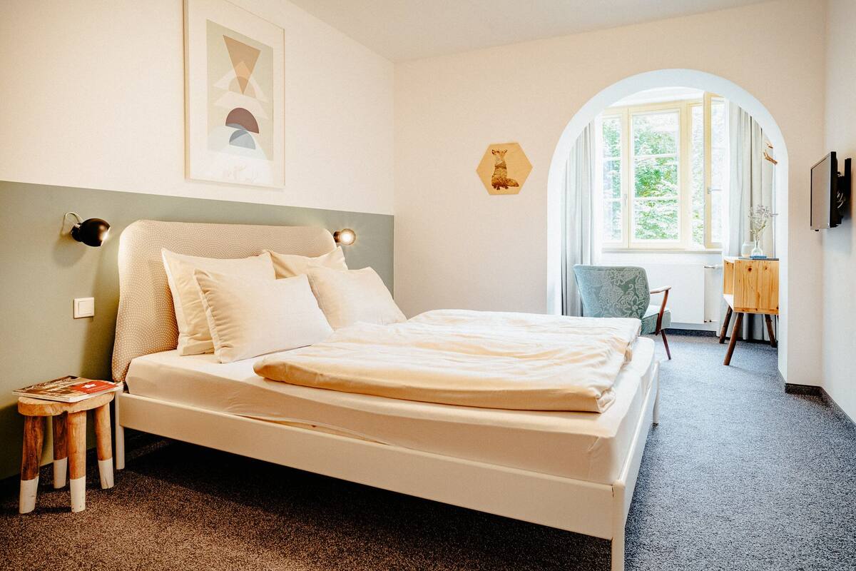 Ein Schlafzimmer mit einem Bett, einem kleinen Tisch, einem Stuhl und einem Schreibtisch mit einer Lampe.
