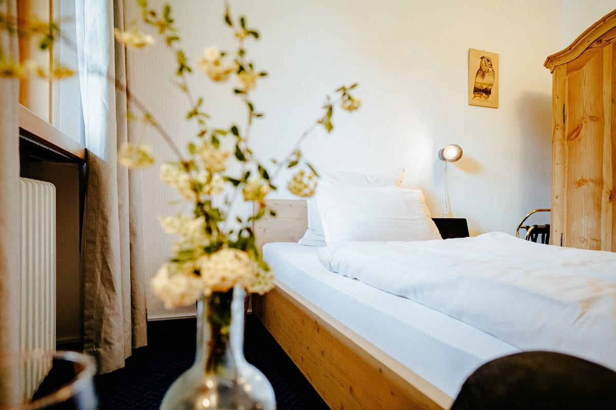 Ein Hotelzimmer mit Bett, Nachttisch, Lampe, einem Holzschrank und einer Vase mit Blumen.