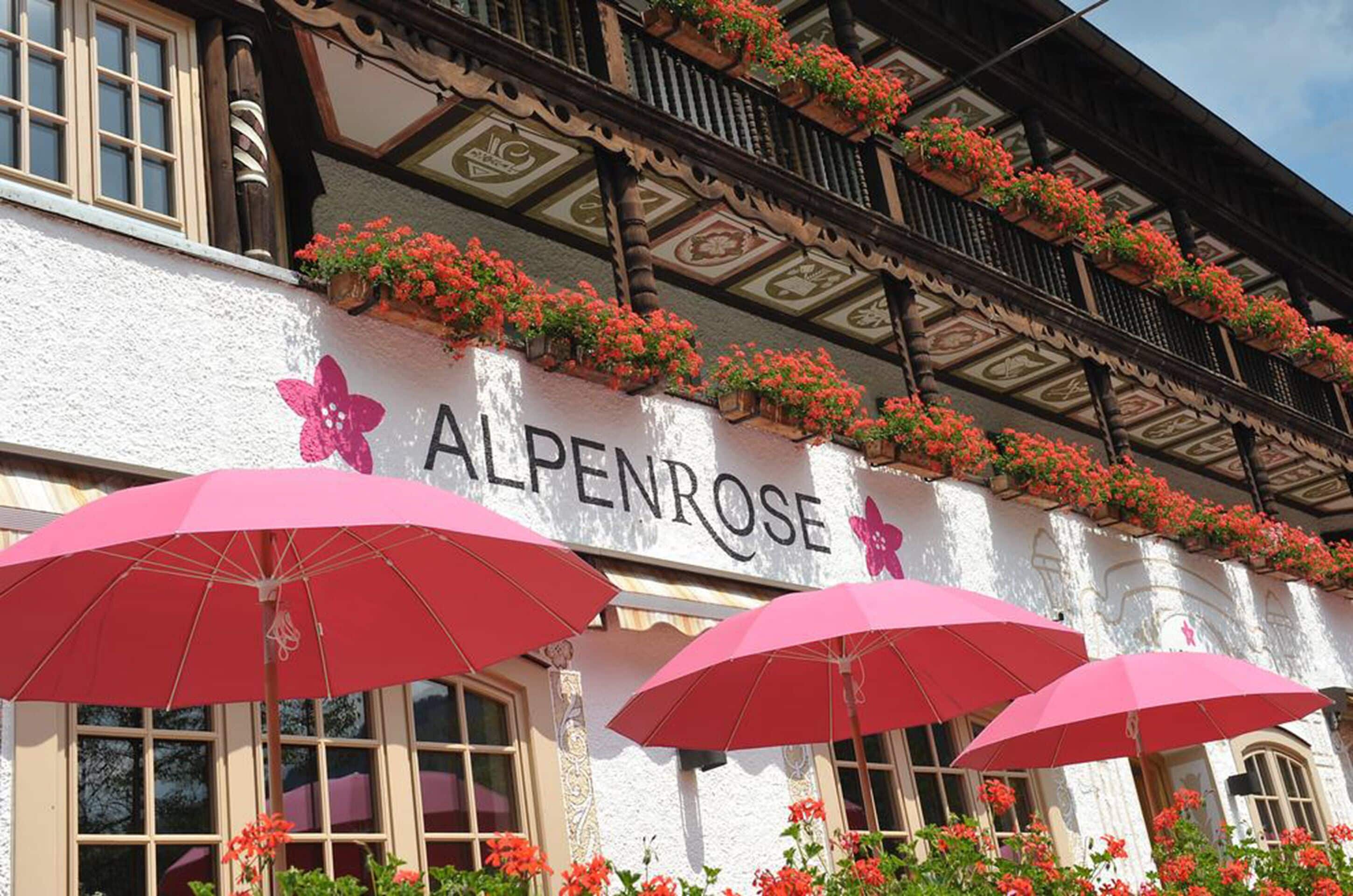 A building with the sign "ALPENROSE" and multiple red umbrellas in front.