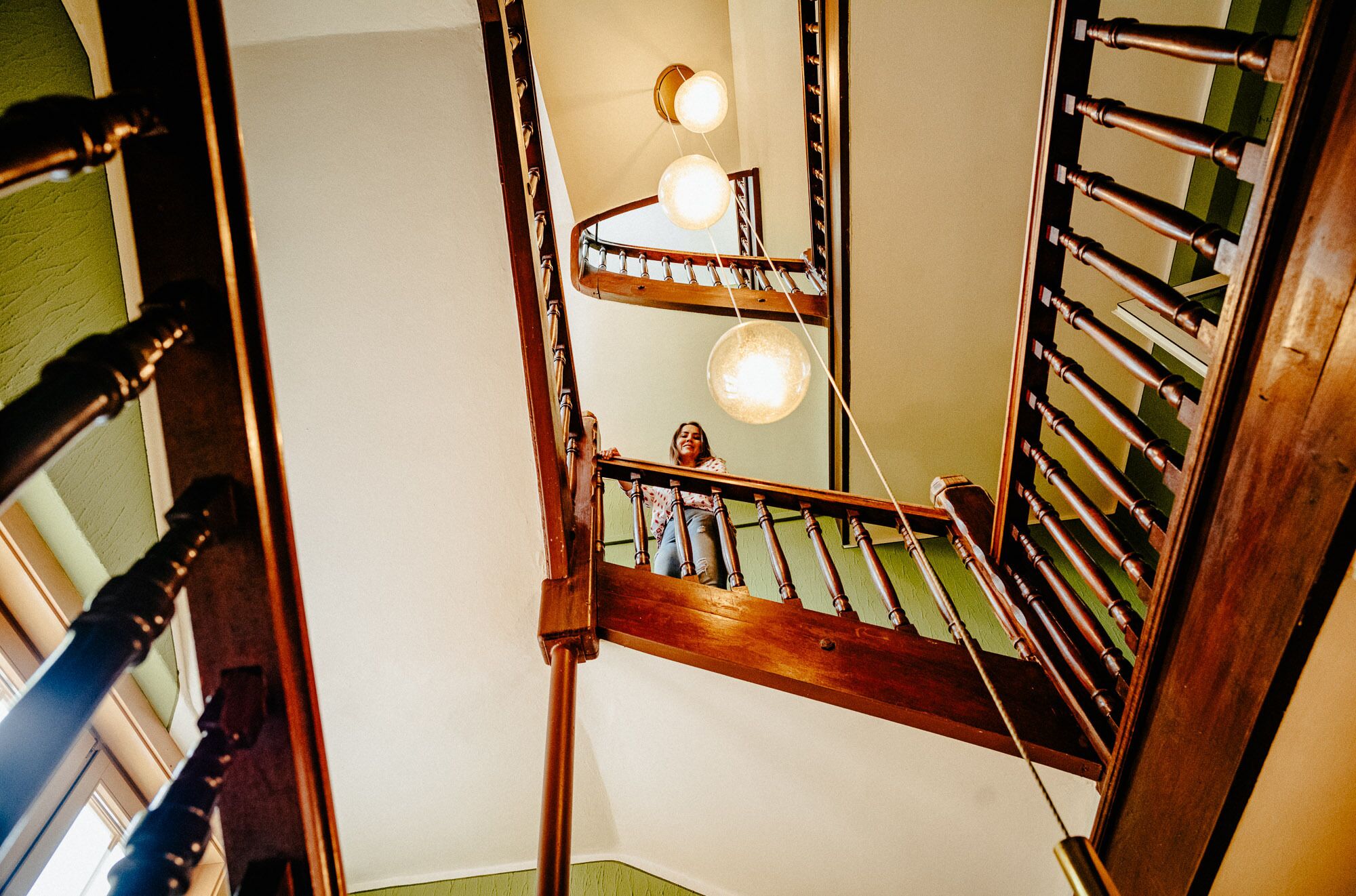 Una escalera de madera con barandilla, una lámpara y un espejo.