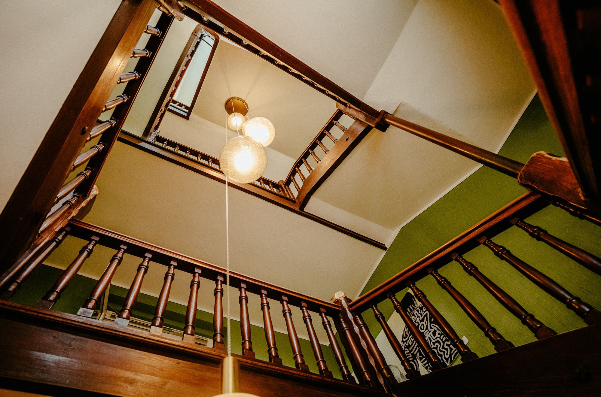 Una escalera de madera con una pared verde y un colgador con luz.
