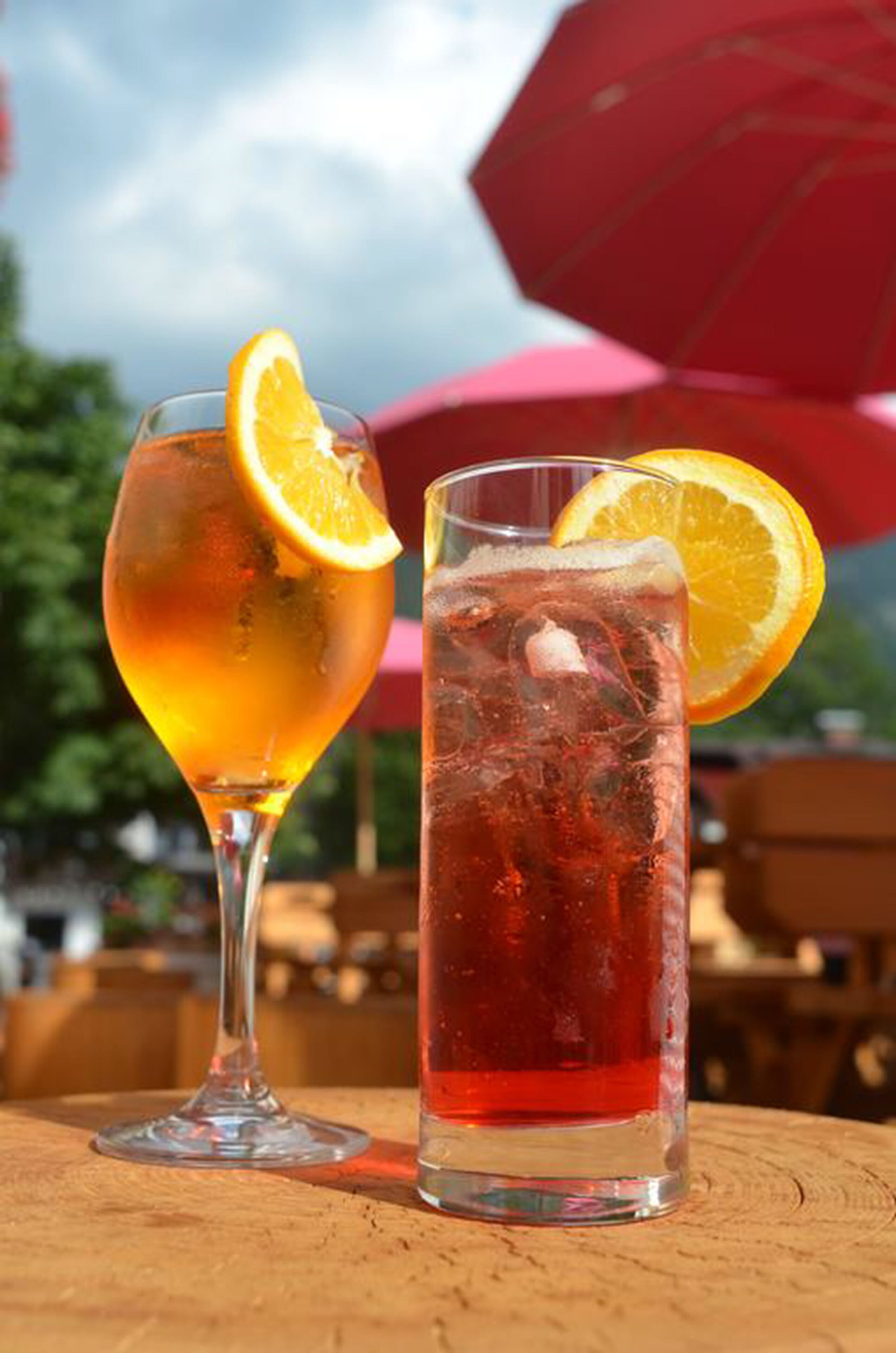 Two drinks on a wooden table with a red umbrella in the background.
