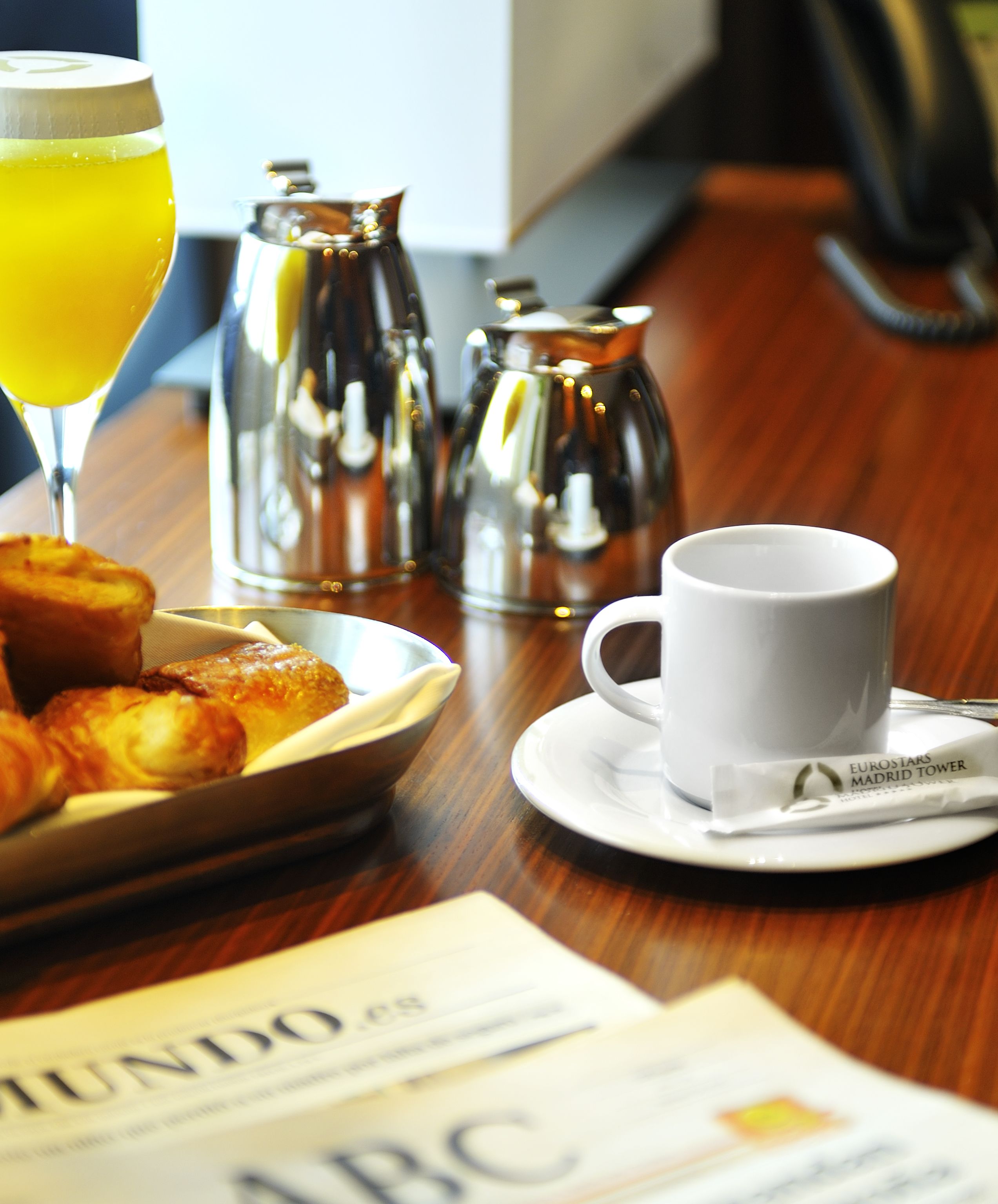 A breakfast table with croissants, a cup of coffee, and a newspaper.