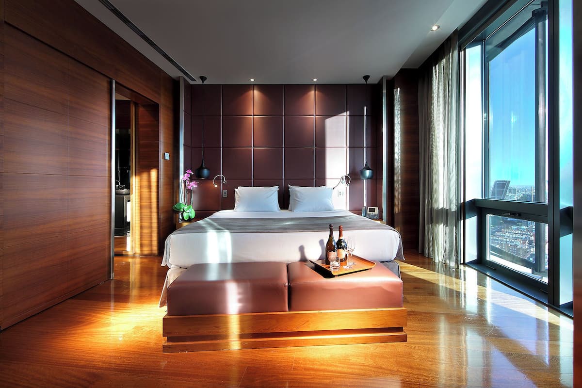 A modern hotel room with a large bed, a wooden floor, and a city view.