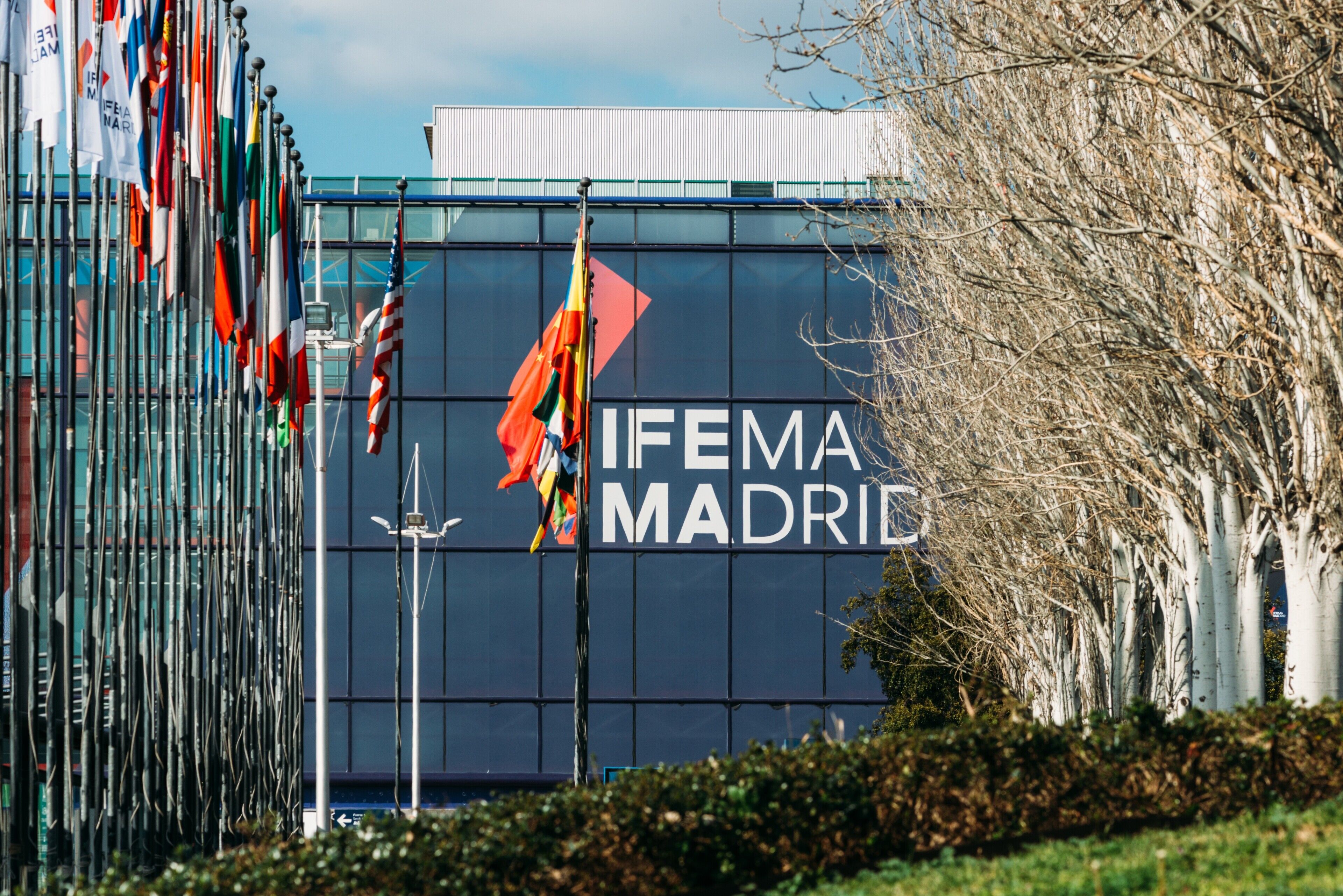 A building with the text "IFEMA MADRID" on its facade, surrounded by multiple flags.