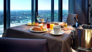 Une table de petit-déjeuner avec vue sur la ville, comprenant un verre de jus d’orange, une tasse de café et divers éléments pour le petit-déjeuner.