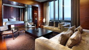 Une chambre d’hôtel moderne, dotée d’un grand lit, d’un canapé, d’une table basse et offrant une vue sur la ville grâce à de grandes fenêtres.